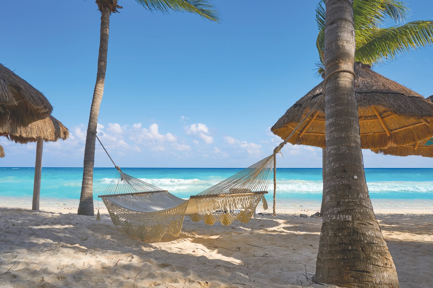 Weißer Sandstrand mit türkisblauem Meer in der Karibik unter klarem Himmel.